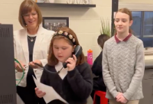 Principal looks on while two students read poems during morning announcements