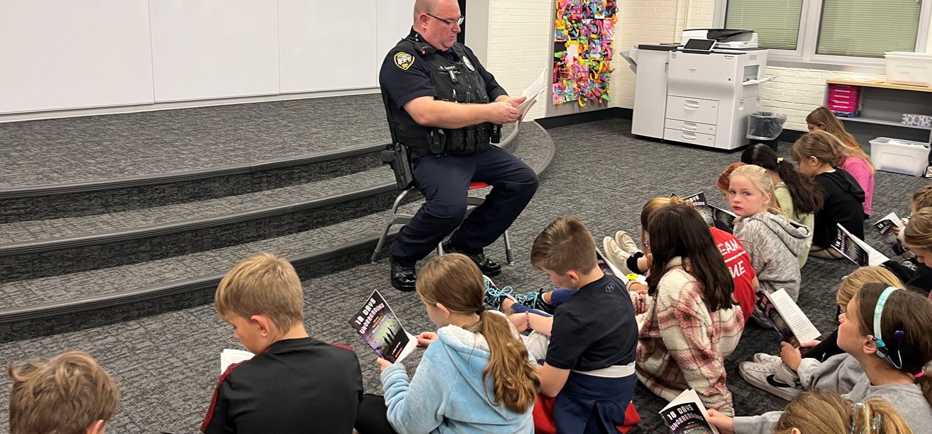 Johnstown Police officer reads book along with students in JIS media center.