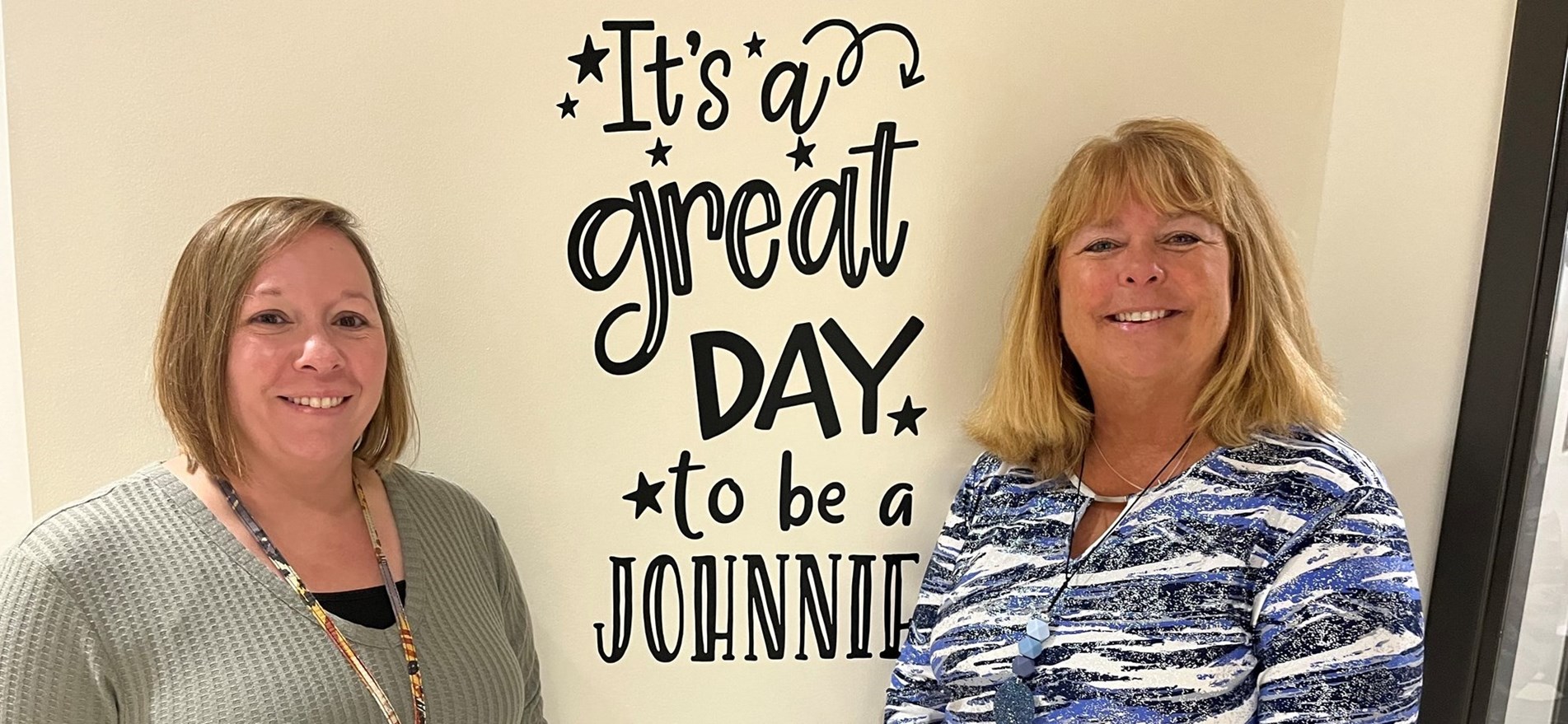 JES Dean of Students and Principal stand by wall decal declaring &#34;IT&#39;s A Great Day To Be A Johnnie!&#34;