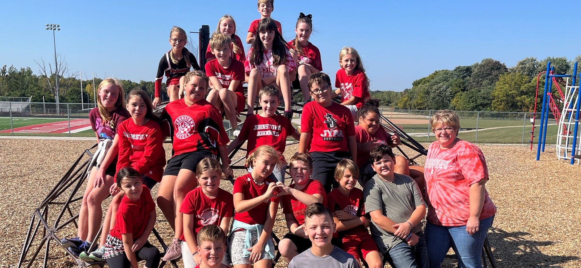 JIS students and teacher dressed in spirit wear gather on jungle gym for a group photo behind school.