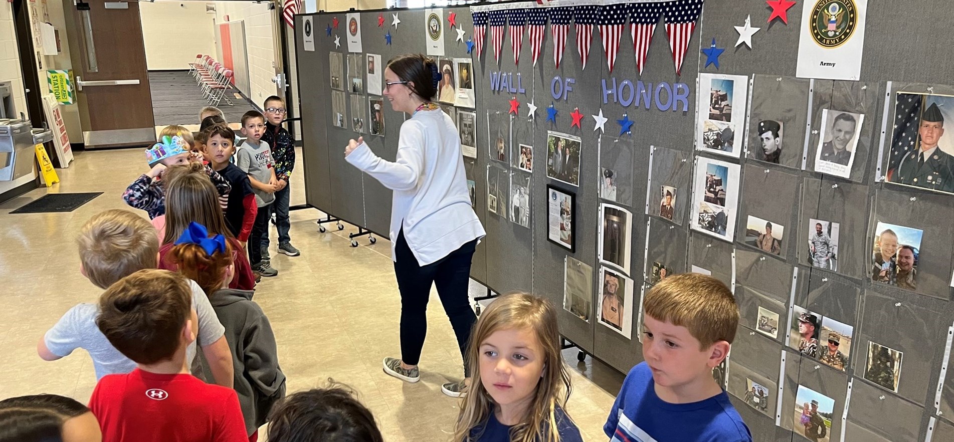 Teacher and students survey Wall of Honor featuring military family veterans photos