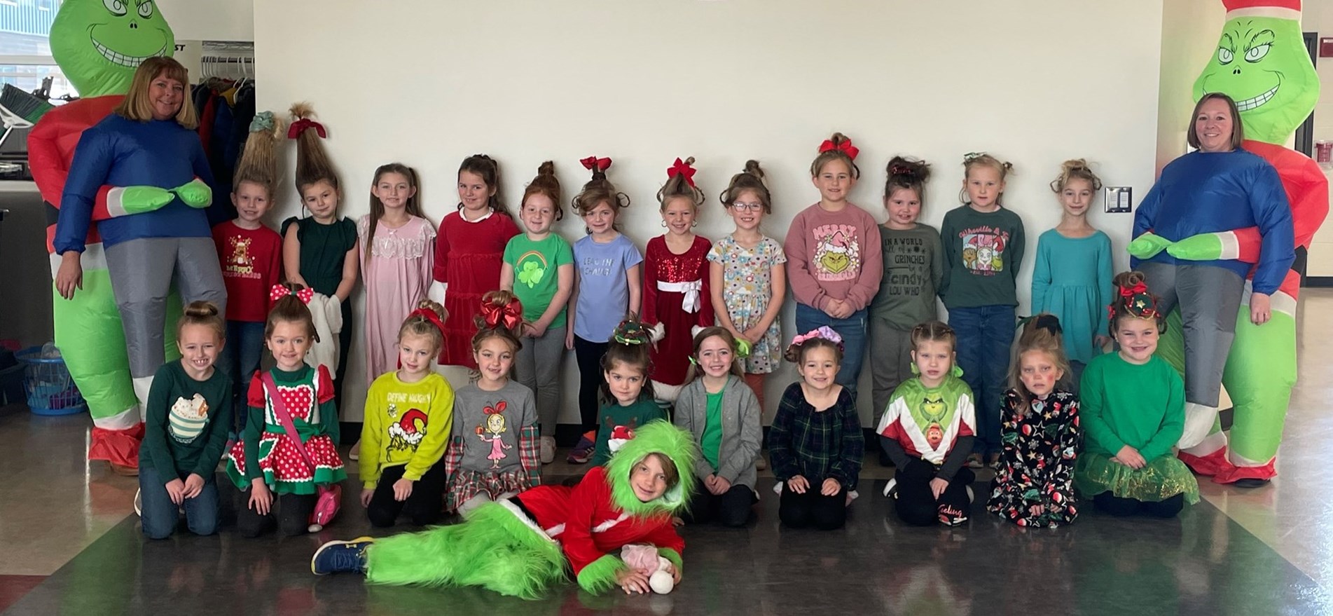 Principal and students dressed as characters from &#34;The Grinch&#34; and stand by wall.