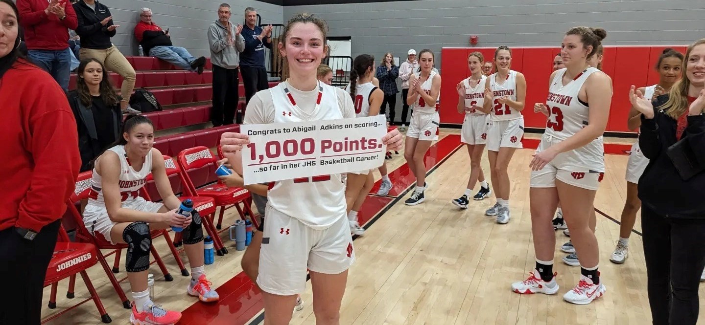 During game break, JHS Girls Basketball team member Abigail Adams holds banner noting scoring of 1,000 points so far over H.S. career