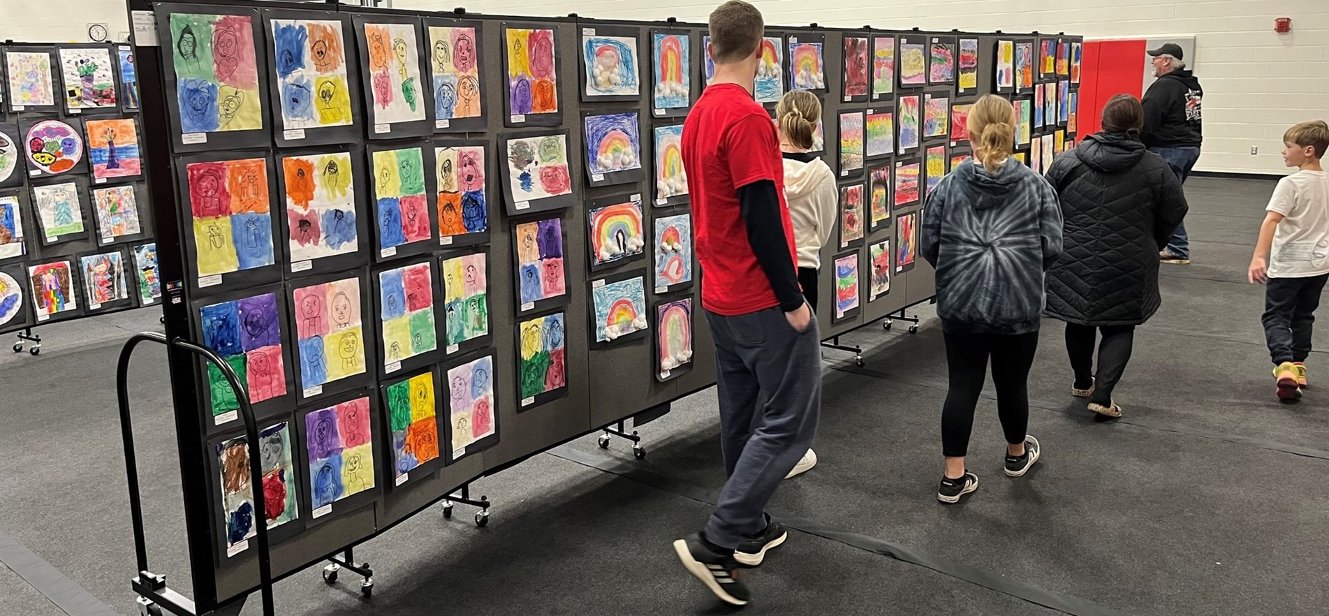 Families tour gym where boards are set up with displayed student art