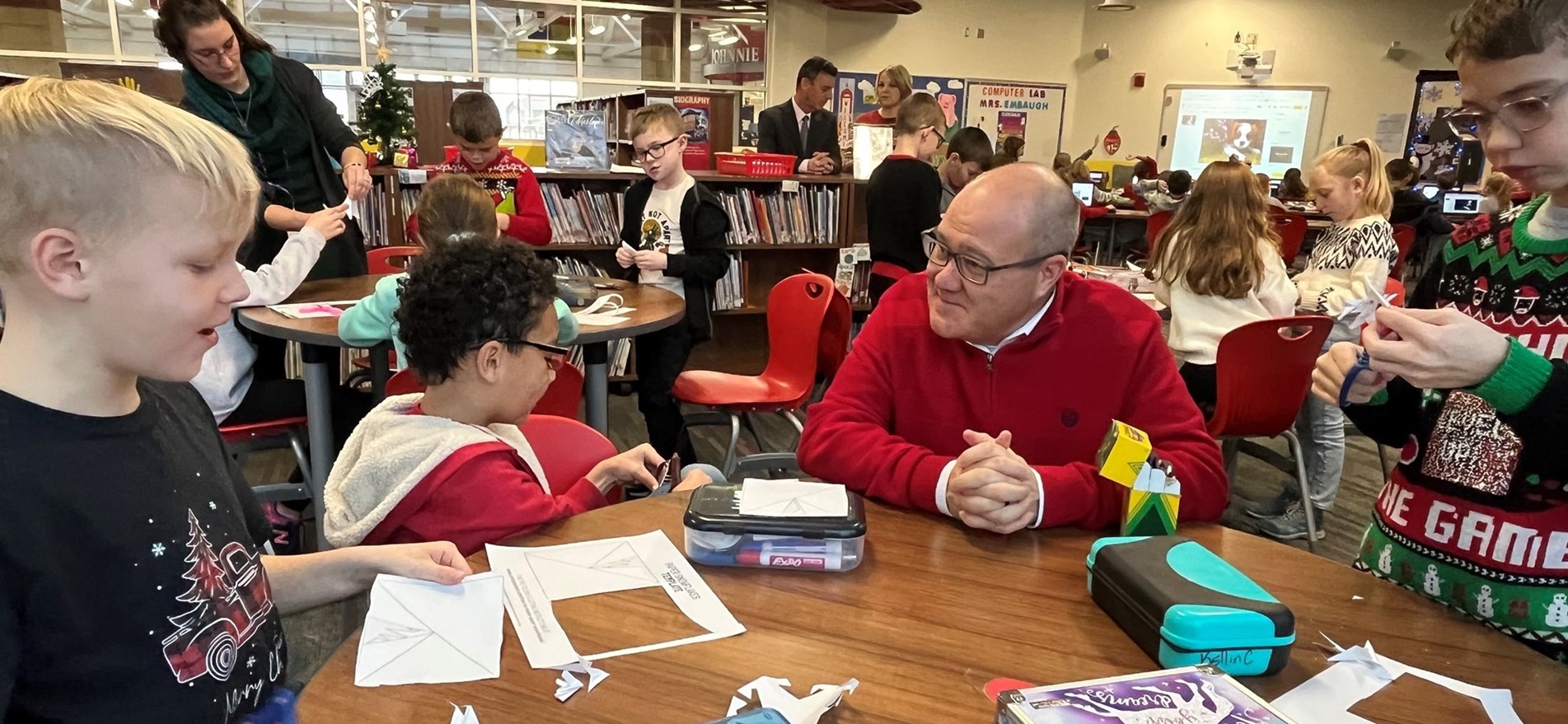 Johnstown Mayor seated with students wearing holiday sweaters in Elementary Media Center