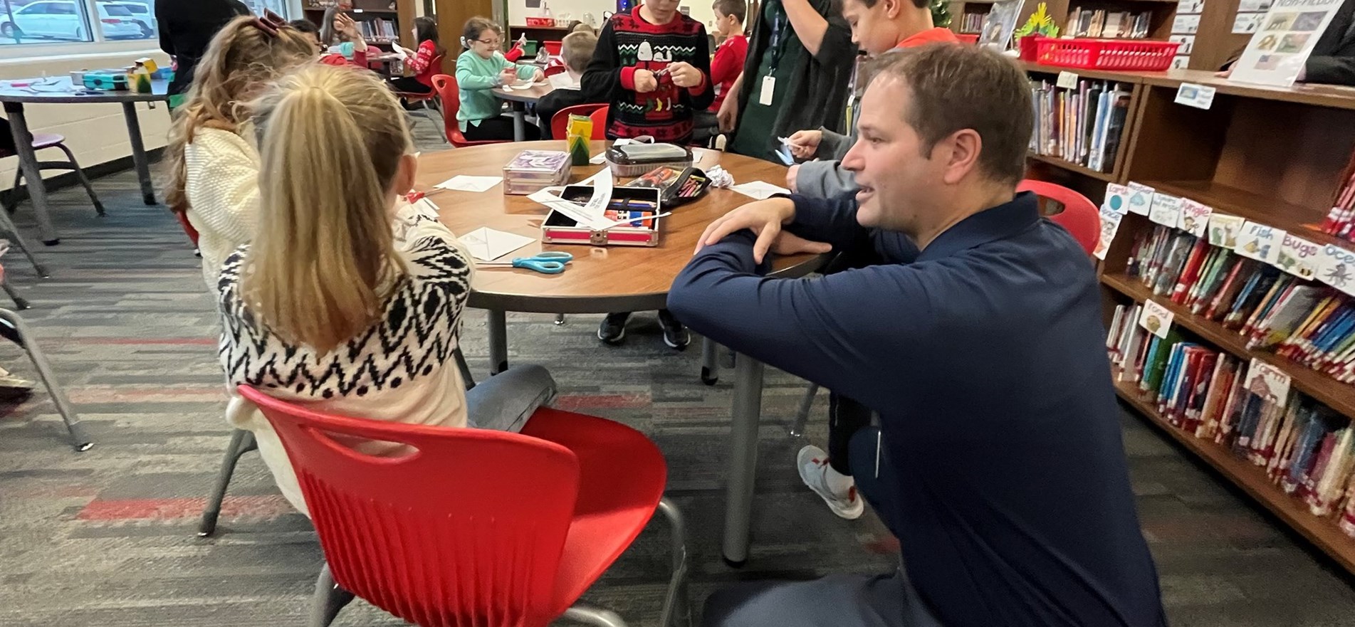 Board member speaks with students during December visit in school media center.